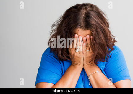Close up of Hispanic woman covering face with hands Stock Photo