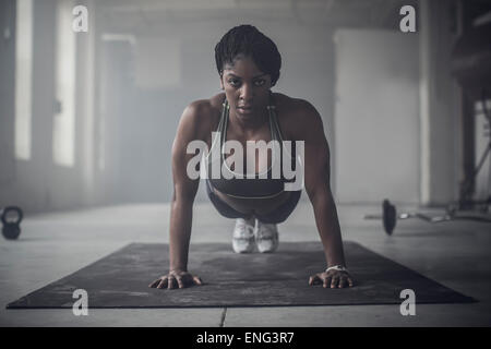 Black woman doing push-ups in dark gym Stock Photo