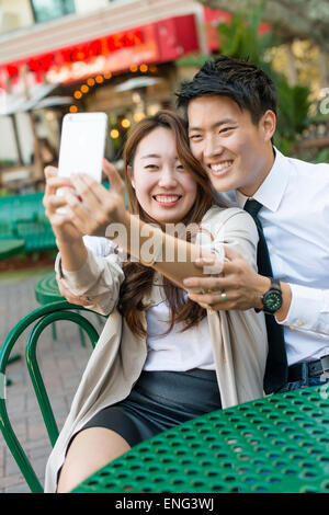 Korean couple taking cell phone photograph at sidewalk cafe Stock Photo