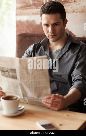 Man reading newspaper and drinking coffee in cafe