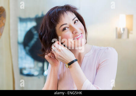 Hispanic woman putting on earrings in mirror Stock Photo