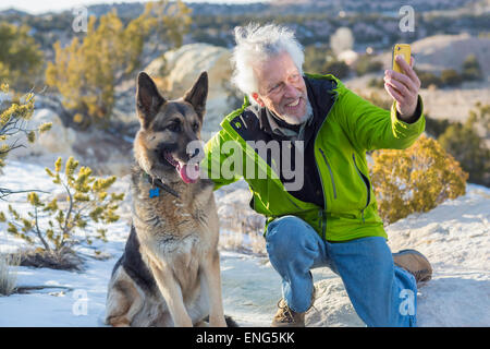 Older man taking cell phone photograph with dog on rock formations Stock Photo