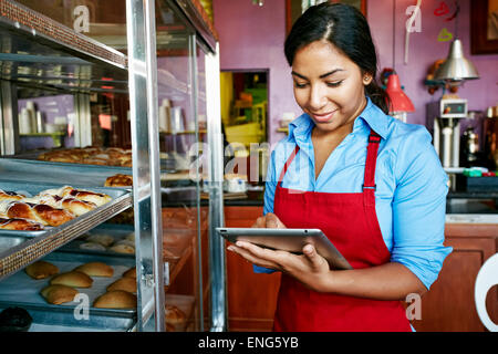 Hispanic waitress taking inventory with digital tablet in bakery Stock Photo