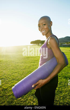 African American woman carrying yoga mat in park Stock Photo