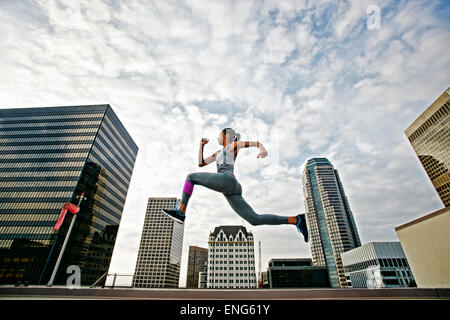 African American woman leaping on urban rooftop Stock Photo