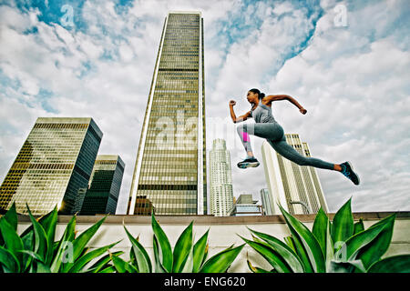 African American woman leaping on urban rooftop Stock Photo
