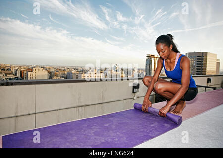 African American woman rolling yoga mat on urban rooftop Stock Photo