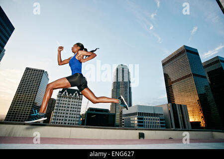African American woman leaping on urban rooftop Stock Photo
