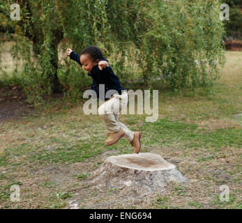 African American boy playing on stump in park Stock Photo