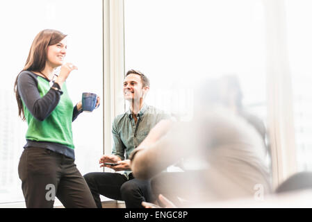 A man and woman holding a cup of coffee talking in an office. Stock Photo