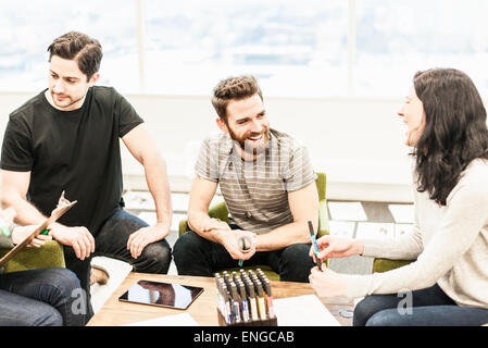 Four people seated at a table, colleagues at a planning meeting holding coloured pens and working on paper and tablets. Stock Photo
