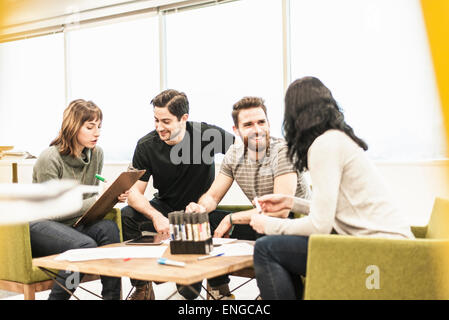 Four people seated at a table, colleagues at a planning meeting holding coloured pens and working on paper and tablets. Stock Photo