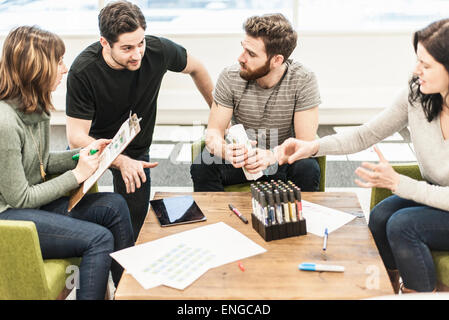 Four people seated at a table, colleagues at a planning meeting holding coloured pens and working on paper and tablets. Stock Photo