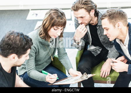 Four people, colleagues at a meeting, and one man writing with a green sharpie on a clipboard. Stock Photo