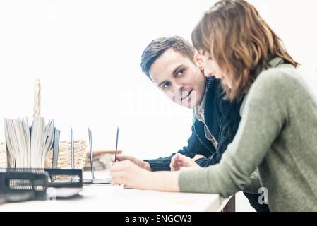 A man and a woman seated side by side talking at a desk in an office. Stock Photo