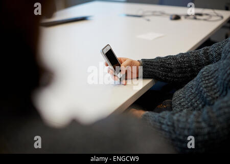 A man seated at a table in an office using his smart phone. Stock Photo