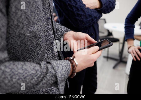 Three people standing in an office, one holding a smart phone. A standup meeting. Stock Photo