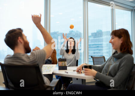 Three business people, two women and a man, reaching up to catch a ball. Stock Photo