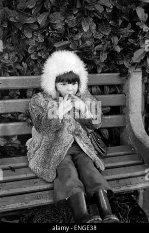 young girl sat on a park bench whistling in the 1970s england uk Stock Photo