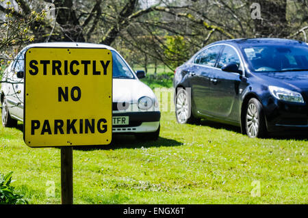 Sign warning people 'Strictly no parking', with two cars parked on the grass Stock Photo