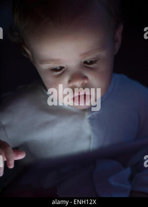 one year old baby boy in a white sleepsuit looking at a tablet computer Stock Photo