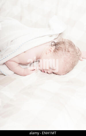 Curly haired Caucasian toddler boy asleep on bed with wet hair after a bath Stock Photo