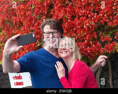 'SELFIE' Attractive couple having fun on holiday taking a 'selfie' photo outside holiday attraction on their iPhone camera application Stock Photo