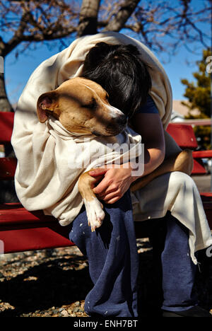 Man sleeping on bench wrapped in blanket holding a dog Stock Photo