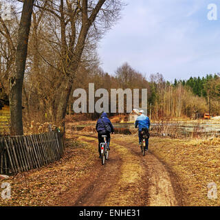 Village spring landscape. Bicyclists on grass road. Stock Photo