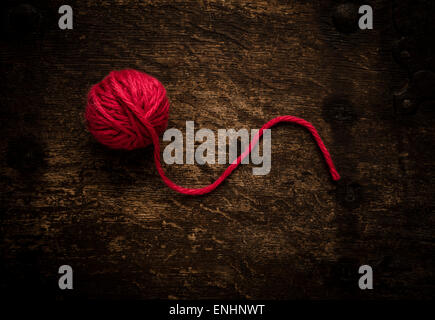 Still life of ball of red yarn on wooden table. Conceptual image of knitting or crocheting. Stock Photo