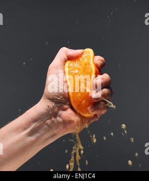 Male hand squeezing juicy orange, dark background Stock Photo