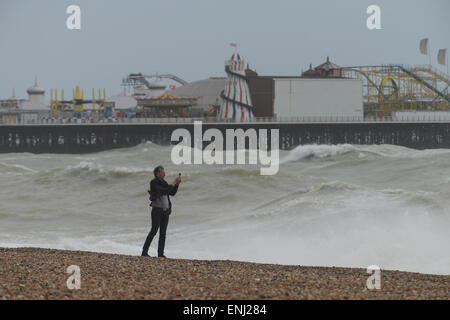 A man takes a photograph of the large waves, caused by a storm, crashing onto the beach in front of Brighton Pier in Brighton, East Sussex, England. Stock Photo