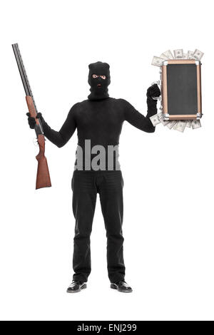 Full length portrait of a masked criminal holding a briefcase full of money in one hand and a shotgun rifle in the other Stock Photo