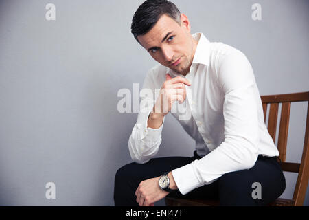 Portrait of a businessman sitting on the chair over gray background and looking at camera Stock Photo