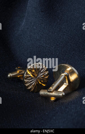 22ct Gold plated Cuff Links with a decorative diamond cut pattern on a dark suit jacket background, shot in natural light. Stock Photo