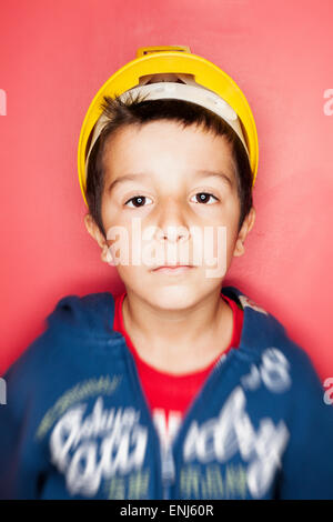 Boy,7,in hard hat against red wall Stock Photo