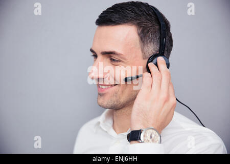 Happy businessman with headphones standing over gray backgorund and looking away
