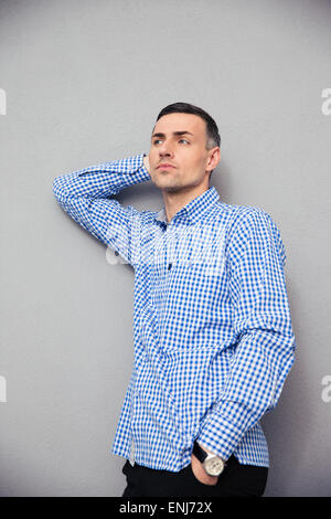 Portrait of a pensive young man in shirt standing over gray background. Looking away Stock Photo