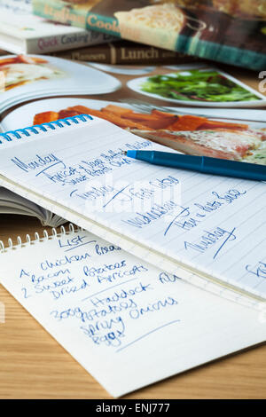 A notepad with weekly meal plan and shopping list on a table top amongst cookery books. Stock Photo