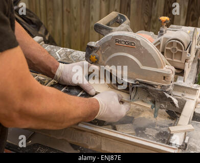 ARLINGTON, VIRGINIA, USA - Worker wearing latex gloves cuts ceramic tiles with a wet tile saw. Stock Photo