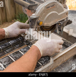 ARLINGTON, VIRGINIA, USA - Worker wearing latex gloves cuts ceramic tiles with a wet tile saw. Stock Photo
