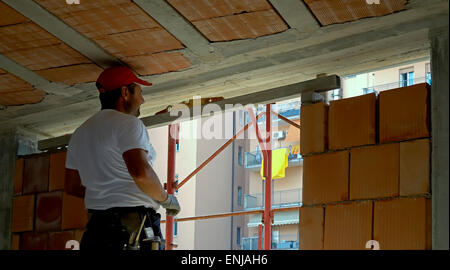Mason standing on a scaffolding and istalling a lintel, using a spirit level and a measuring cord for alignment. Shot of the con Stock Photo