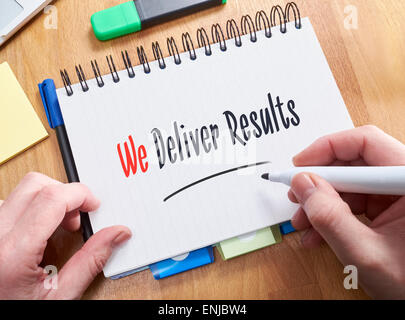 A businessman writing the words,  We Deliver Results, on a note pad. Stock Photo