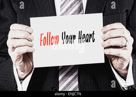 A businessman holding a business card with the words, Follow Your Heart, written on it. Stock Photo