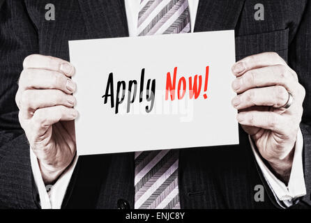 A businessman holding a business card with the words,  Apply Now, written on it. Stock Photo