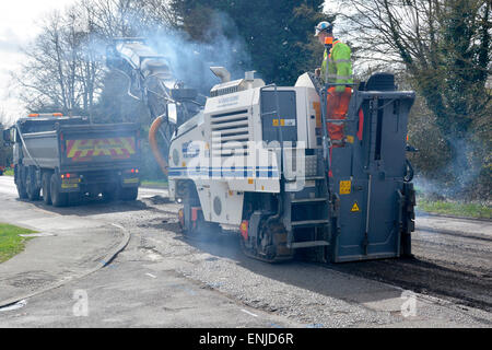 Defective & worn out asphalt road being planed off in preparation for repaving tipper truck loading waste for recycling Brentwood Essex England UK Stock Photo