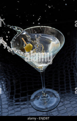 Splashing dirty martini garnished with green olives on toothpick Stock Photo