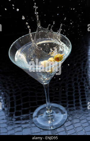 Splashing dirty martini garnished with green olives on toothpick Stock Photo