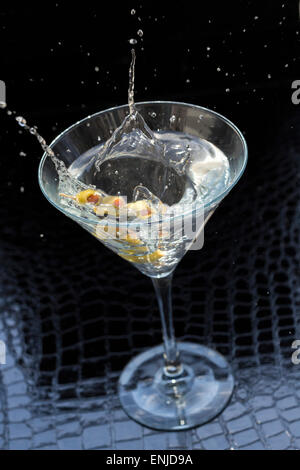 Splashing dirty martini garnished with green olives on toothpick Stock Photo