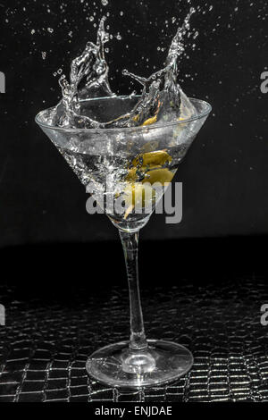 Splashing dirty martini garnished with green olives on toothpick Stock Photo